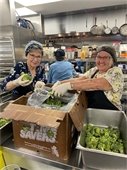 Two smiling volunteers cooking broccoli at The Humanity Alliance.