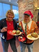 Couple wearing holiday sweater smile holding their baked potatoes.