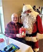 Man smiles with Santa after winning the cookie jar at the Lodge Holiday Party.